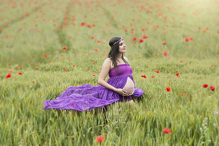 pregnant woman in purple dress in the middle of grass field thumbnail