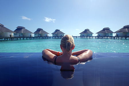 selective focus photography of woman swimming on pool facing white huts thumbnail