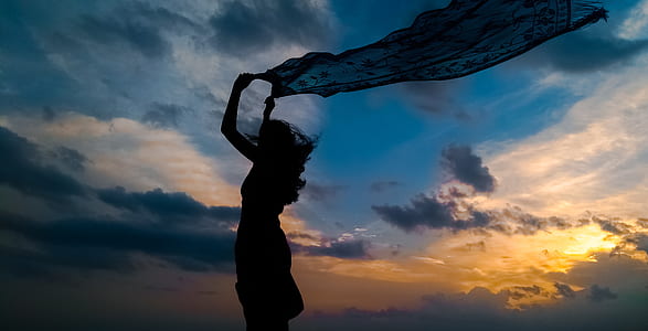 silhouette of woman holding blue dress during sunset thumbnail