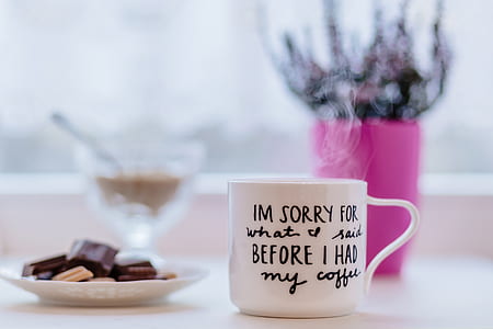 white and black printed ceramic mug near white plate with chocolates on top place on table thumbnail