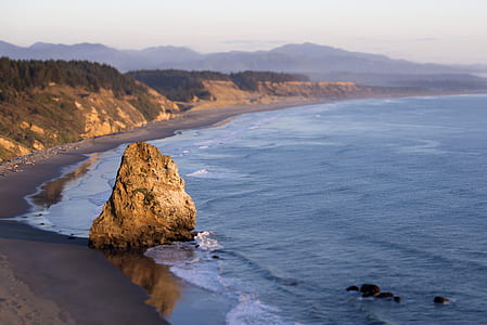 boulder by the shore overlooking mountains and body of water during sunrise thumbnail