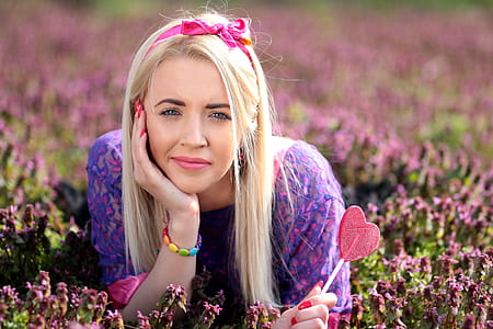woman lying on pink petal flower field while holding candy thumbnail