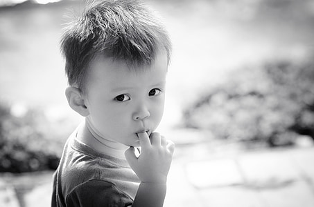 grayscale photography of boy wearing crew-neck shirt eating his finger thumbnail