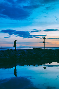 silhouette of walking woman on stones near ocean at daytime thumbnail