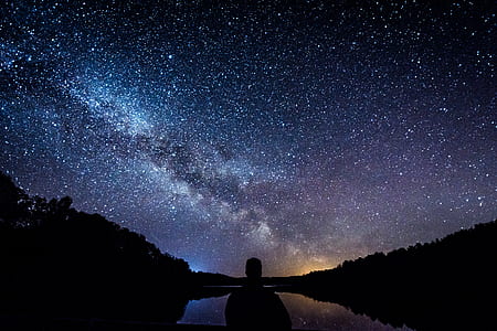 silhouette of person near body of water under starry night thumbnail