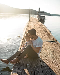 man in white shirt sitting on brown wooden dock at daytime thumbnail