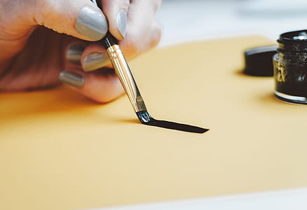 person holding black paintbrush painting line beside ink well thumbnail