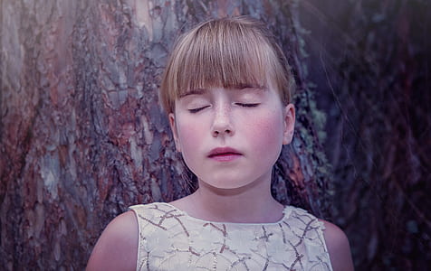 girl wearing white and gray crew-neck sleeveless top leaning on brown tree thumbnail