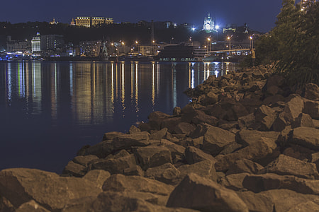 rocks near body of water and city during night time thumbnail