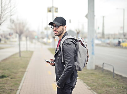 Young Adult bearded male backpacker with backpack on his shoulders seen listening to music in his cellphone thumbnail