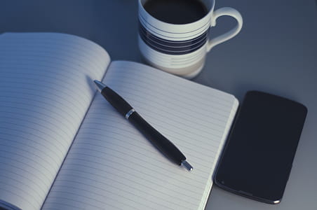 clear black-lined white notebook near pen and coffee mug thumbnail