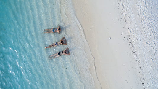 bird's eye photography of three persons in beach laying on their stomachs thumbnail