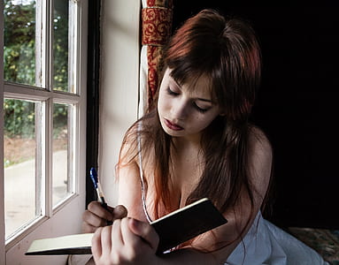 woman writing in open book in front of white window thumbnail