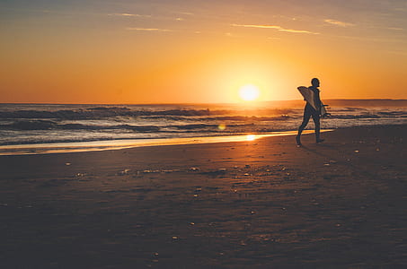 silhouette photograph of person waling on beach with surfboard thumbnail
