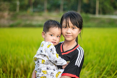 girl carrying baby on grass field thumbnail