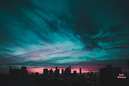 silhouette of city buildings under teal and pink cloudy sky thumbnail