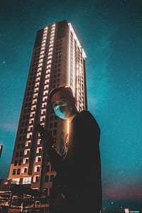 man wearing mask standing near concrete building thumbnail
