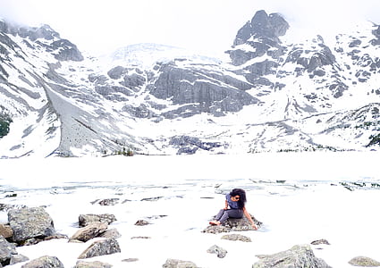 woman sitting on rock in front of mountain coated with snow thumbnail