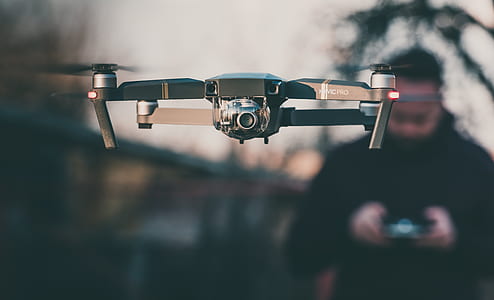 black quadcopter drone with camera controlled by man in black jacket selective-focus photography thumbnail