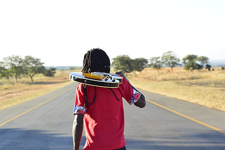 man holding guitar while standing on road during daytime thumbnail