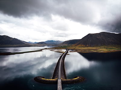 road bridge near mountains under cloudy sky thumbnail