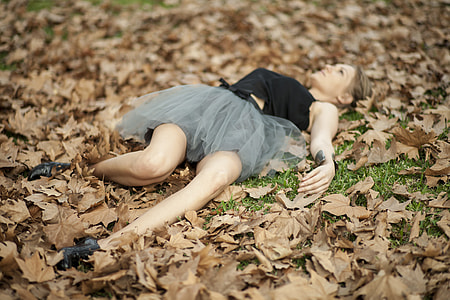woman in black and gray tulle dress lying on pile of withered leaves thumbnail