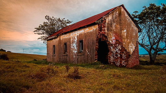 brown house with red roof and two trees at the back under blue and orange sky during golden hour thumbnail
