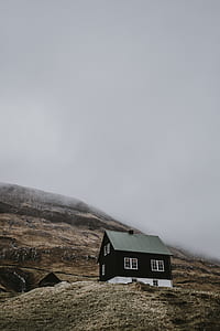 photo of black and white wooden house on brown hill under blue clouds at daytime thumbnail