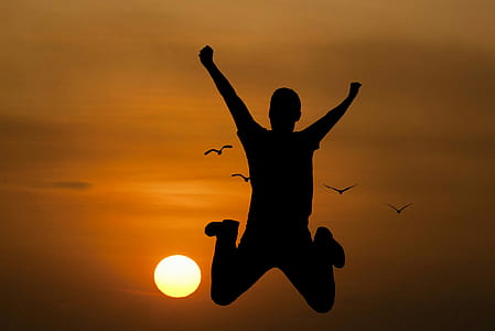 Silhouette of young man jumping with setting sun in background. thumbnail