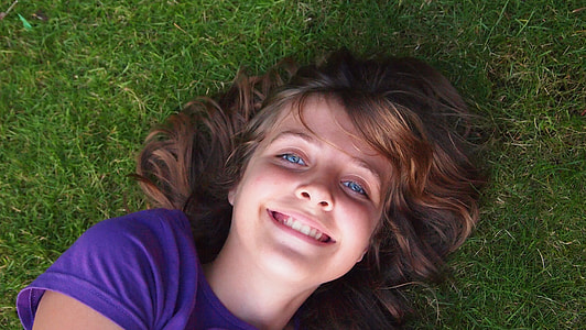girl in purple crew-neck shirt lying on green grass thumbnail