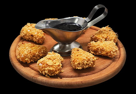 sauce filled gray metal sauce boat surrounded by several fried meat on top of round brown wooden board thumbnail