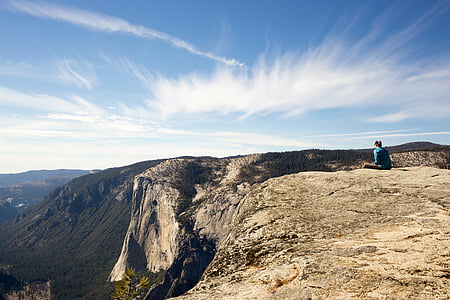 person sitting on cliff under blue skies thumbnail