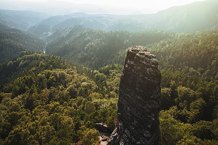 black and gray rock formation in the middle of green trees under blue sky and white cloud thumbnail