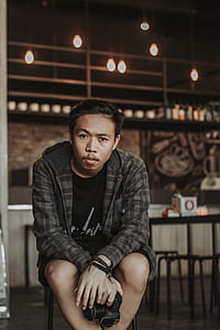 man sitting on brown wooden stool holding DSLR camera thumbnail