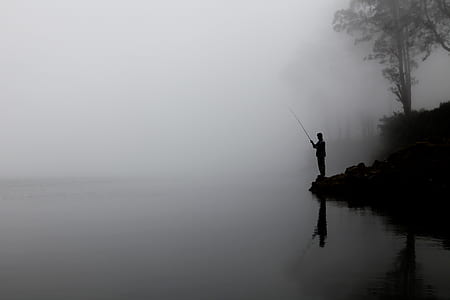 silhouette photography of person fishing beside river surrounded by mist thumbnail