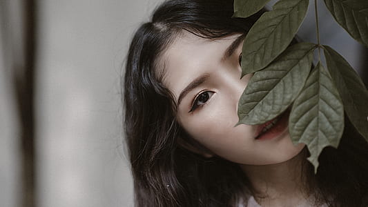Woman With Black Hair Peeking Through Green Leaves thumbnail