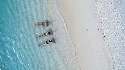 three women wearing bikinis lying on beach thumbnail