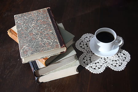 filled white cup on top of white saucer near four piled books thumbnail