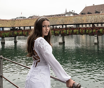 woman wearing white applique long-sleeved strappy-back dress holding gray metal railings near body of water thumbnail