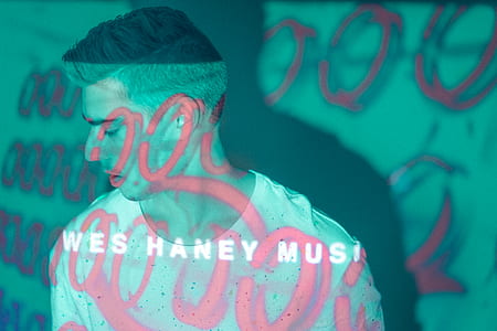 man in white shirt standing under pink and green lights thumbnail