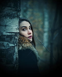 woman wearing black and brown parka jacket with red lipstick leaning on brown tree trunk thumbnail