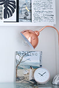 brass-colored study lamp and white analog desk clock on table beside book thumbnail