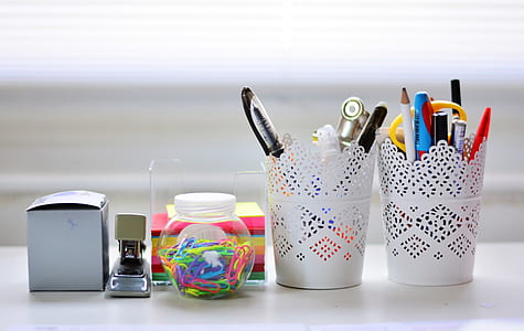 pens, pencils, and scissors inside pen rack with paper clips in jar, sticky notes and stapler on white surface thumbnail