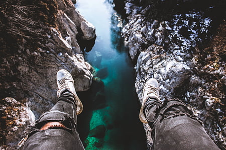 man sitting on edge of cliff looking on body of water during daytime thumbnail