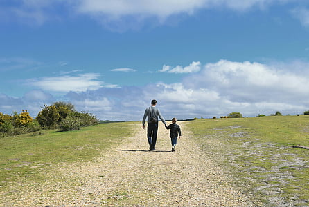 man holding children while walking on green grass field thumbnail
