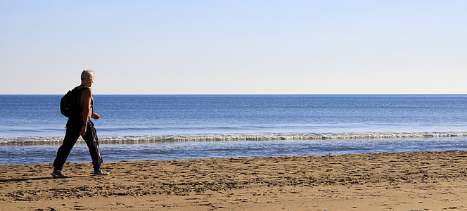 man walking beside body of water under blue and white sky during daytime thumbnail