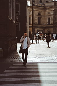 man talking over phone walking on pedestrian lane surrounded by high-rise buildings thumbnail