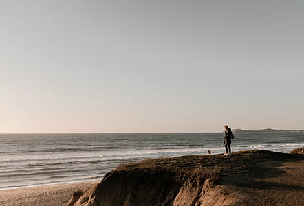 man standing on rock cliff near ocean thumbnail