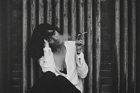 woman in white long-sleeved shirt and black pants sitting and holding cigarette thumbnail