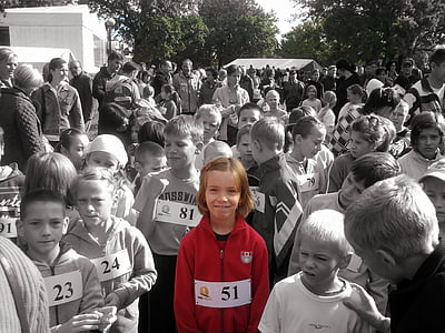 selective-color photography of child wearing red zip-up hooded jacket beside crowd of people during daytime thumbnail